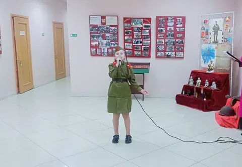 Девочка в гимнастёрке поёт в зале выставки