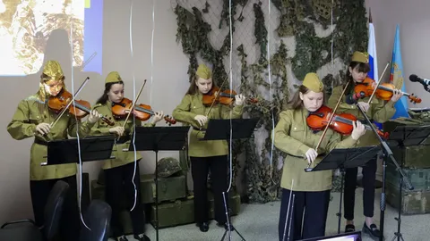 Ансамбль скрипачей в гимнастёрках и пилотках на фоне маскировочной сети