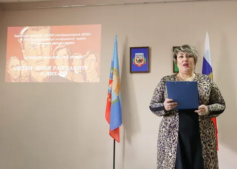 Ведущая с папкой в руках, на экране — заставка экскурса