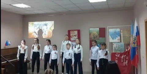 Дети в белых рубашках поют перед экраном