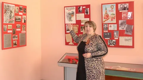Ведущая рассказывает о выставке у стенда с документами